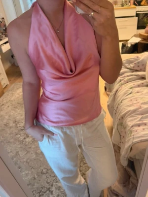 Rosa halterneck topp i satin - Säljer en snygg rosa halterneck topp i satin med draperad front och öppen rygg. Toppen knyts både i nacken och ryggen för en justerbar passform. Perfekt för dig som vill ha en trendig och somrig look.