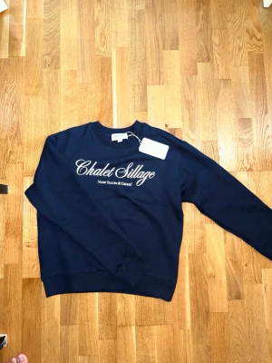 OANVÄND Notre Succès tröja - Oanvänd mörkblå sweatshirt från Notre Succès med trycket 'Chalet Sillage' på bröstet i vit text. Tröjan är helt oanvänd och har kvar lappen. Hög kvalitet.