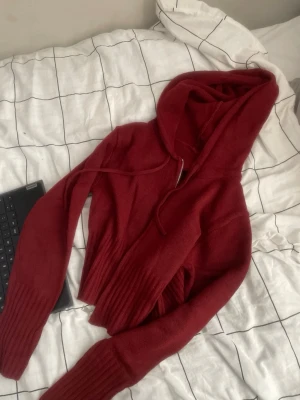 Vinröd hoodie med dragkedja - Snygg vinröd hoodie med dragkedja framtill och ribbade muddar vid ärmar och midja. Hoodien har en stor huva och dragsko. Perfekt för en avslappnad och trendig look. Materialet ser mjukt och bekvämt ut.