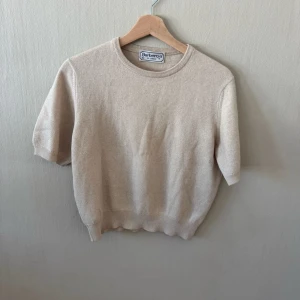 Beige kortärmad topp från Burberry - Säljer en stilren beige topp från Burberry i mjukt material. Toppen har rund halsringning, korta ärmar och ribbade kanter. Perfekt att matcha med jeans eller kjol för en clean look.0119