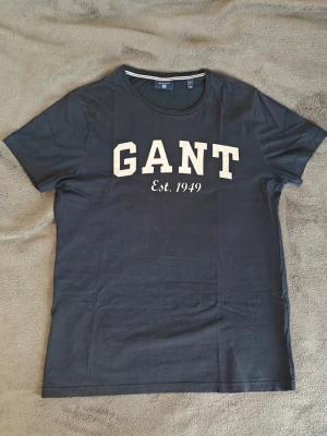 Marinblå Gant thsirt - Gant thsirt tillverkad i mjukt bomull och har ett stort "GANT" tryck framtill. Storlek S och bra passform. Kontakta för fler bilder, info eller frågor! 😁