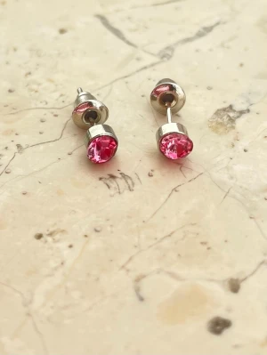 Silverfärgade örhängen med en rosa sten  - Silverfärgade örhängen med rosa sten. Obs! Inte silver eller äkta sten. Material okänt. Helt nya aldrig använda.