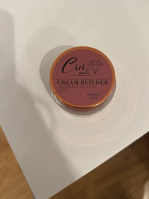 Cici Nails Cream Builder Caramel Nude - Cici Nails Cream Builder i färgen Caramel Nude är en professionell nagelgel för att bygga och forma naglar. Kommer i en rund burk med rosa och guld detaljer. Perfekt för dig som vill skapa naturliga och snygga naglar med en nude-ton. 30g endast gjort en test nagel med denna