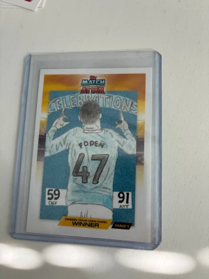 Match Attax samlarkort Foden #47 - Säljer ett Match Attax samlarkort med spelaren Foden, nummer 47, från 'Design Your Own Card'-tävlingen. Kortet har färgglad illustration, texten 'Celebrations' och är inplastat. Perfekt för dig som gillar fotboll och unika samlarkort.