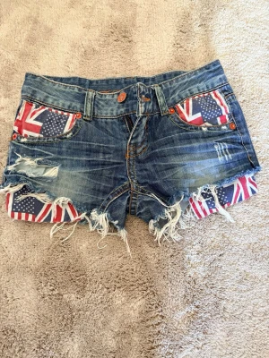 Blå jeansshorts med flaggdetaljer - Säljer vintage shorts som inte finns någonstans. Passar ej längre. Superfina 