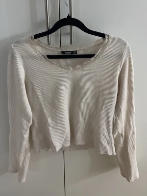 Creme vit  ribbad långärmad topp - Söt creme vit ribbad långärmad topp från busem med spetsdetalj runt den rundade halsringningen.  