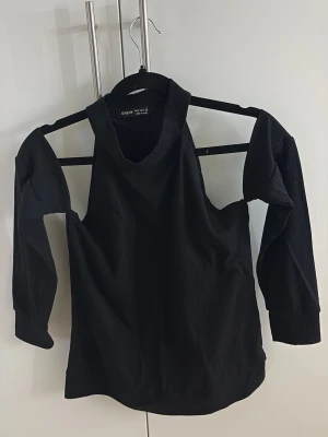 Svart offshoulder topp - Svart offshoulder topp med långärmad design och ribbad struktur. Toppen har en unik cut-out detalj vid axlarna.