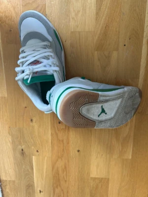 Vita och gröna Air Jordan sneakers - Säljer ett par vita och gröna Air Jordan sneakers med klassisk Jumpman-logga på sulan och tungan. Skorna har vita snören, gråa och gröna detaljer samt en vadderad plös. Materialet är en mix av läder och textil för en sportig look.