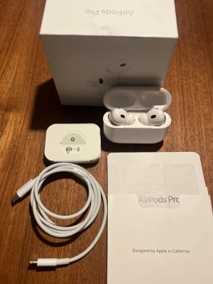 Apple AirPods Pro  - Säljer ett par vita Apple AirPods Pro gen 2 med trådlöst laddningsetui. Inkluderar USB lightning laddningskabel, extra öronproppar och originalförpackning. Snygg och stilren design i plast, perfekt för musik och samtal. 