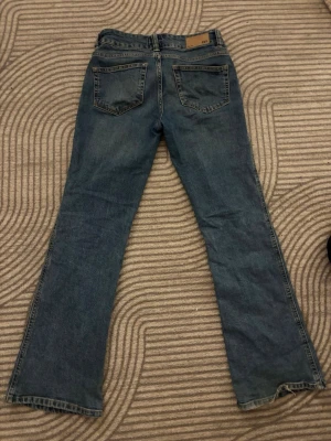 Blå bootcut jeans med låg midja - Säljer ett par klassiska blå bootcut jeans med låg midja och fem fickor. Jeansen har en lätt tvättad look och raka ben som går ut något nedtill. Materialet är denim i bomull.