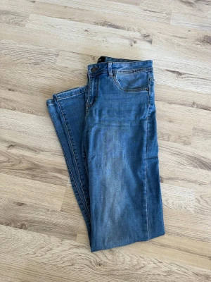 Blå raka jeans med fem fickor - Snygga blå jeans med klassisk femficksmodell och raka ben. Jeansen har en lätt tvättad look med subtila slitningar framtill och stängs med knapp och dragkedja. Perfekta till vardagsstilen och passar till det mesta. Materialet är denim i bomull.