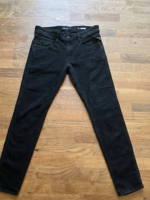 Svarta anbass jeans från Replay - Snygga svarta anbass jeans från Replay med klassisk femficksdesign och smal passform. Jeansen har normal midja, dragkedja och knappstängning samt diskreta detaljer vid fickorna. Perfekta för en stilren och modern look.