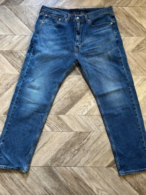 Levi's 505 - Klassiska blå jeans från Levi's med rak passform och fem fickor. Jeansen har en snygg tvätt med lätt slitning på låren och bakfickor med den ikoniska röda Levi's-lappen. Tillverkade i slitstark denim, perfekta för en avslappnad stil.