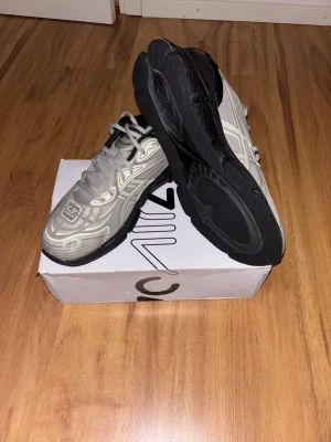 Asics Gel-Quantum 360 C.P. Company - Snygga grå sneakers från CP Company med vita detaljer och svart sula. Skorna har ett futuristiskt mönster på ovandelen och klassisk snörning. Perfekta för dig som gillar streetwear och vill sticka ut lite extra.