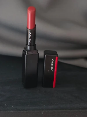 Shiseido VisionAiry Gel Lipstick 227 - Shiseido VisionAiry Gel Lipstick i nyansen 227 Sleeping Dragon. Läppstiftet har en djup röd ton med en lätt gel-formula som ger en mjuk och krämig känsla på läpparna. Hylsan är svart med en röd detalj och elegant Shiseido-logga.