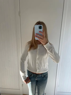 Vit kofta  - Söt vit kofta med rund hals och långa ärmar. Koftan har knappar framtill och ribbade muddar vid ärmslut och nederkant. Perfekt att slänga över en topp eller bära stängd för en clean look.