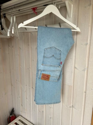 Ljusblå raka Levi's jeans - Säljer ett par klassiska ljusblå Levi's jeans med raka ben och femficksmodell. Jeansen har den ikoniska läderlappen bak och röd Levi's-tag på bakfickan. Perfekta för en avslappnad och trendig look. Tillverkade i slitstark denim. Storlek 27/30🩵