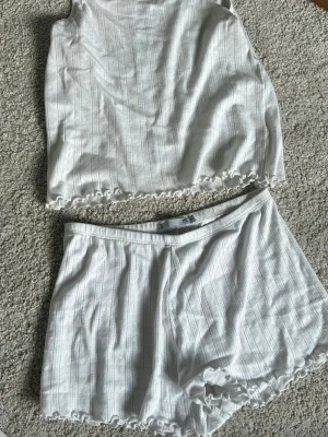Vitt ribbat pyjamasset linne & shorts - Säljer ett vitt pyjamasset med linne och shorts i mjukt ribbat material. Båda delarna har vågig kant och ett diskret hålmönster i tyget. Perfekt för dig som gillar bekväma och luftiga underkläder med enkel design.