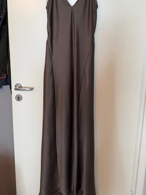Grå/Silvrig långklänning i satin - Elegant grå/silvrig aftonklänning i satin med v-ringning och smala axelband. Klänningen har en slät, glansig yta och öppen rygg.