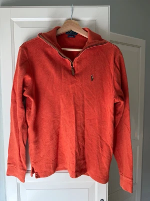 Polo Ralph Lauren halfzip - Snygg orange långärmad tröja från Polo Ralph Lauren med halv dragkedja och klassisk broderad logga på bröstet. Tröjan har en avslappnad passform och är tillverkad i mjukt material, perfekt för lager på lager under kyliga dagar.