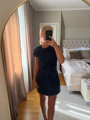 Mörkblå ärmlös jeansklänning - Säljer en snygg mörkblå jeansklänning i kort modell. Klänningen är ärmlös med rund halsringning och har en figurnära passform. Perfekt för dig som gillar en enkel men trendig look. Materialet är kraftigt denim som ger en cool känsla.