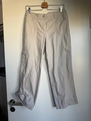 Beiga cargobyxor med raka ben - Snygga beiga cargobyxor med raka ben och flera fickor på sidorna. Byxorna har en avslappnad passform och är tillverkade i ett lätt och svalt material, perfekt för en chill och trendig look. Stängs med knapp och dragkedja framtill.