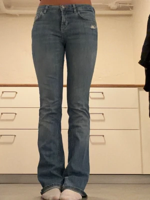 Utsvängda blå jeans från Zara - Säljer ett par blåa utsvängda jeans med liten slitning vid fickan. Jeansen har låg midja och stängs med dragkedja och knapp. Dessa jeans är använda men fortfarande i ett bra skick💕💕