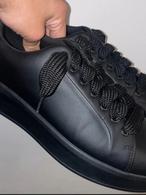 Svarta chunky sneakers med breda snören - Stilrena helsvarta sneakers med chunky sula och breda, grova snören. Skon är tillverkad i slätt konstläder och har en minimalistisk design utan synliga loggor eller detaljer. Perfekt för dig som gillar en clean och modern look.