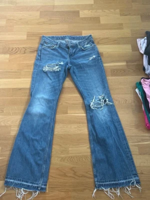 Blå slitna bootcut jeans med hål - Säljer ett par blå bootcut jeans med slitningar och hål på knäna och låret. Från weekday i strl 26/32 men uppsprättda. Hålen också egengjorda men super fint gjorda och skick.