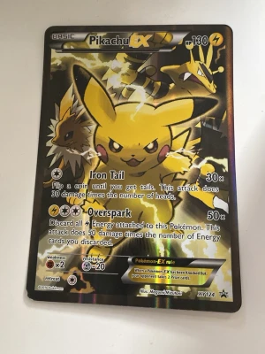 Pikachu EX Pokémonkort XY124 - Unikt Pikachu EX samlarkort från Pokémon-serien, nummer XY124. Kortet har en glansig yta med motiv av Pikachu och Jolteon i eltema. Text och effekter på engelska, med attacker som Iron Tail och Overspark. Perfekt för samlare eller Pokémonfans.