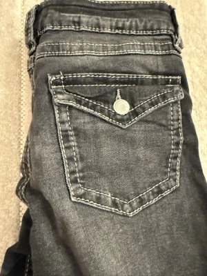 Svarta bootcut jeans med kontrastsömmar - Snygga svarta jeans med bootcut-modell och tydliga vita kontrastsömmar. Jeansen har en ficka med lock och knapp bak samt klassisk femficksdesign. Materialet är denim med lätt tvättad look för en cool vibe.