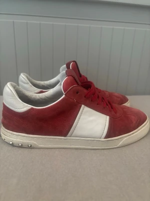 Röda valentino flycrews, 41.5 - Snygga sneakers från Valentino i rött mocka och vitt läder. Skorna har röda skosnören, vita detaljer på sidan och hälen samt nitar på sulan. Perfekta för dig som vill sticka ut med en exklusiv touch och cool design.