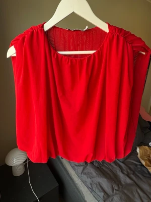 Röd ärmlös topp från NA-KD - Snygg röd topp från NA-KD i storlek XS. Toppen är ärmlös med lös passform och har en rundad halsringning samt lätt rynkade axlar. Materialet är tunt och faller snyggt, perfekt för att skapa en trendig look.