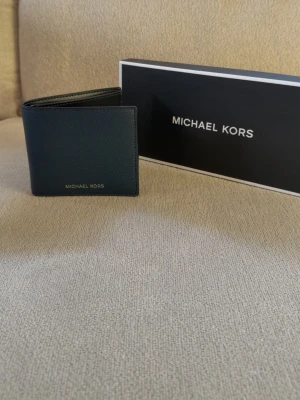 Svart plånbok från Michael Kors - Stilren marinblå plånbok från Michael Kors i slätt läder. Plånboken har flera kortfack på insidan och en klassisk vikbar design. Den är helt ny och oanvänd. Hör av er vid funderingar🙌