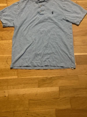 Ljusblå piké t-shirt med knappdetalj - Snygg ljusblå piké t-shirt med korta ärmar och knappdetalj vid halsen. Klassisk passform och diskret logga på bröstet. Perfekt till jeans eller shorts för en avslappnad stil.