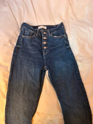 Mörkblå utsvängda jeans från Zara  - Säljer ett par klassiska mörkblå jeans med rak passform. Jeansen har en enkel design utan synliga slitningar eller dekorationer. Perfekta till en avslappnad stil och tillverkade i ett mjukt denimtyg.