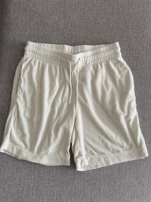 Vita mjuka shorts med snörning - Säljer ett par vita shorts i mjukt frottématerial. De har elastisk midja med snörning och fickor på sidorna samt en bakficka. Perfekta för lata sommardagar eller när du vill chilla hemma.