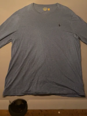 Blå långärmad t-shirt Polo Ralph Lauren - Långärmad t-shirt i ljusblått från Polo Ralph Lauren med klassisk rund halsringning och den ikoniska broderade loggan på bröstet. Tillverkad i mjukt bomullsmaterial och har en slim fit-passform som sitter snyggt på kroppen.