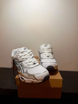Vita Asics sneakers med mesh och silver - Snygga vita sneakers från Asics med detaljer i silver och svart. Ovandelen är i mesh och syntet för en sportig look och bra andningsförmåga. Klassisk snörning och bekväm sula som passar perfekt till streetwear eller casual outfits.