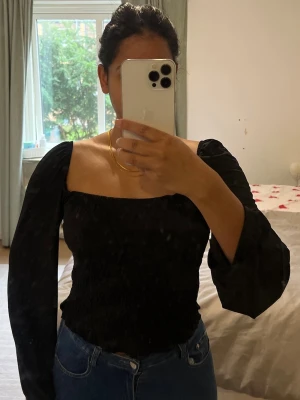 Svart topp från gina tricot - Svart långarmädad blus från gina tricot, storlek m. Passar även för personer i storlek S. Toppen har smockad kropp och är tillverkad i ett mjukt, lätt material som ger en snygg passform. Perfekt att styla med jeans eller kjol för en cool look.