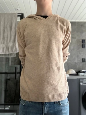 Beige Kashmir tröja  i mjukt material - Säljer en beige hoodie med huva och långa ärmar. Hoodien är tillverkad i ett mjukt, stickat material och har ribbade muddar vid ärmslut och nederkant. Enkel och clean design utan tryck eller logga, perfekt för en avslappnad stil.