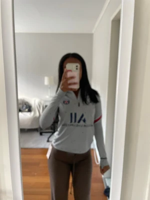 Grå PSG träningströja med dragkedja - Säljer en grå långärmad PSG träningströja från Nike med halv dragkedja framtill. Tröjan har blå och röda detaljer på ärmarna, PSG-logga på bröstet och texten 'VISIT RWANDA' på ryggen. Perfekt för fotbollsträning eller chill dagar.