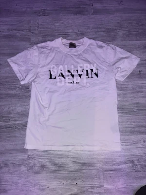Vit Lanvin x Gallery Dept t-shirt - Säljer en vit t-shirt med tryck från Lanvin x Gallery Dept. T-shirten har klassisk passform, rund halsringning och svart samt vitt tryck på bröstet. Perfekt för dig som gillar streetwear och vill ha något stilrent men ändå unikt.