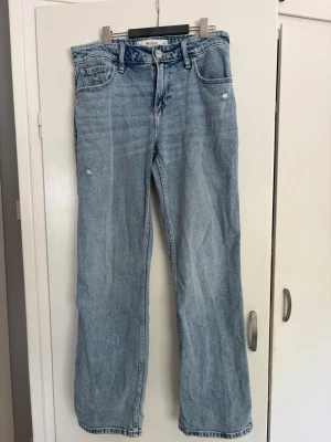 Ljusblå raka jeans med slitningar - Säljer ett par ljusblå jeans med raka ben och små slitningar framtill. Jeansen har klassisk femficksmodell, hög midja och är gjorda i ett mjukt denimtyg. Perfekta för en avslappnad och trendig look. Storlek w27 