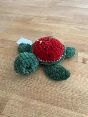 Virkad sköldpadda - Söt liten fruktsköldpadda i mjukt plyschmaterial. Skölden är röd med svarta prickar och kroppen är grön och ska föreställa en vattenmelon. Perfekt som dekoration eller leksak. Lätt att hålla i handen och supergosig.