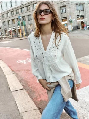 Vit blus med broderade detaljer - Säljer en luftig vit blus med v-ringning och broderade detaljer framtill. Blusen har långa ärmar med knappar vid ärmslut och en avslappnad passform. Perfekt till jeans för en trendig vardagslook.