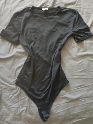 Svart body från Amisu med kort ärm - En enkel och stilren svart body från Amisu i storlek M. Bodyn har korta ärmar, rund halsringning och är tillverkad i ett mjukt stretchigt material som sitter snyggt på kroppen. Perfekt att matcha med jeans eller kjol.