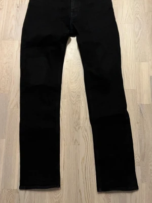 Svarta raka jeans från Hugo Boss - Säljer ett par svarta jeans med rak passform och klassisk femficksdesign. Jeansen har normal midja och är tillverkade i ett mjukt denimtyg som ger en clean look. Perfekta för dig som gillar stilrena och enkla plagg.