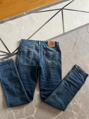 Levis 512 Slim Taper - Säljer ett par klassiska blå skinny jeans från Levi's med fem fickor och snygga kontrastsömmar. Jeansen har normal midja och en liten röd Levi's-tag på bakfickan. Perfekta för en avslappnad och trendig look.