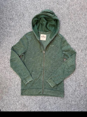 Grön zip hoodie från Hollister - Säljer denna Snygga gröna hoodie från Hollister i jätte bra skick och till bra pris,         Skick 9/10. Storlek S men sitter lika bra som en M Bara att skriva vid några funderingar!